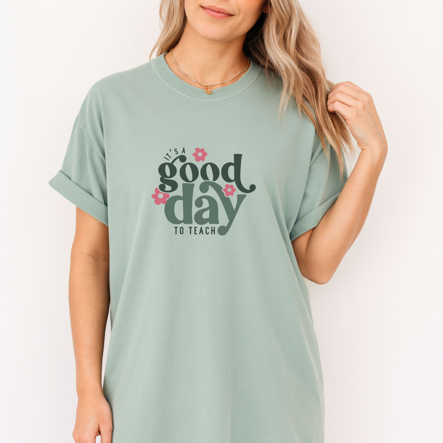 Person wearing a light green t-shirt with 'It's a good day to teach' text and flowers on a white background