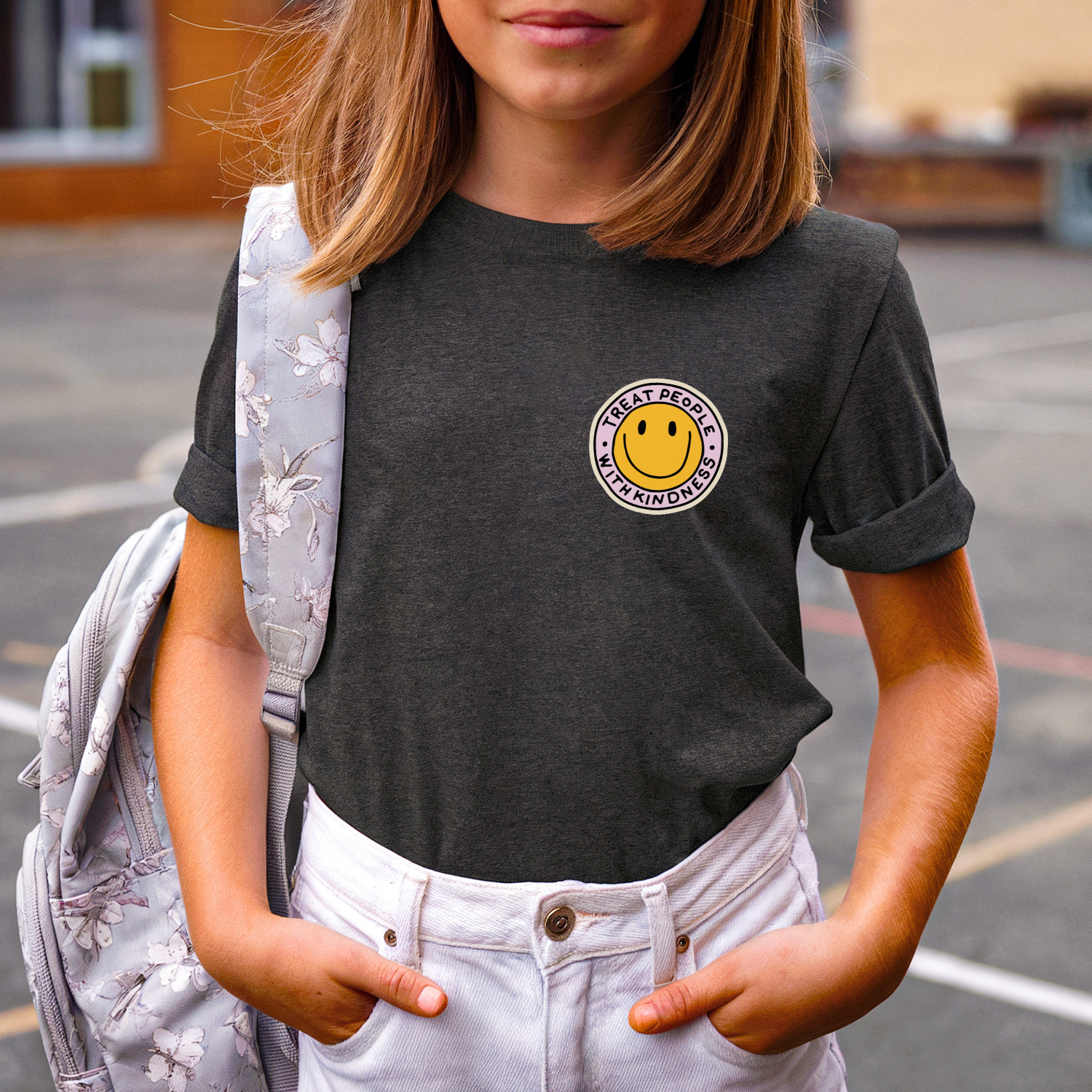 Person wearing a dark gray t-shirt with a smiley face logo, standing outdoors.