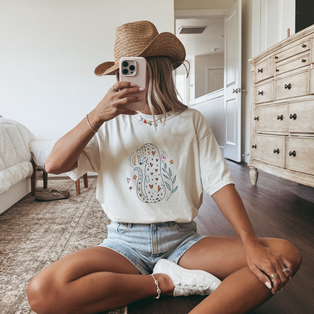 Girl with straw hat and ivory colored tee with a cute hand drawn boho illustration of a leopard