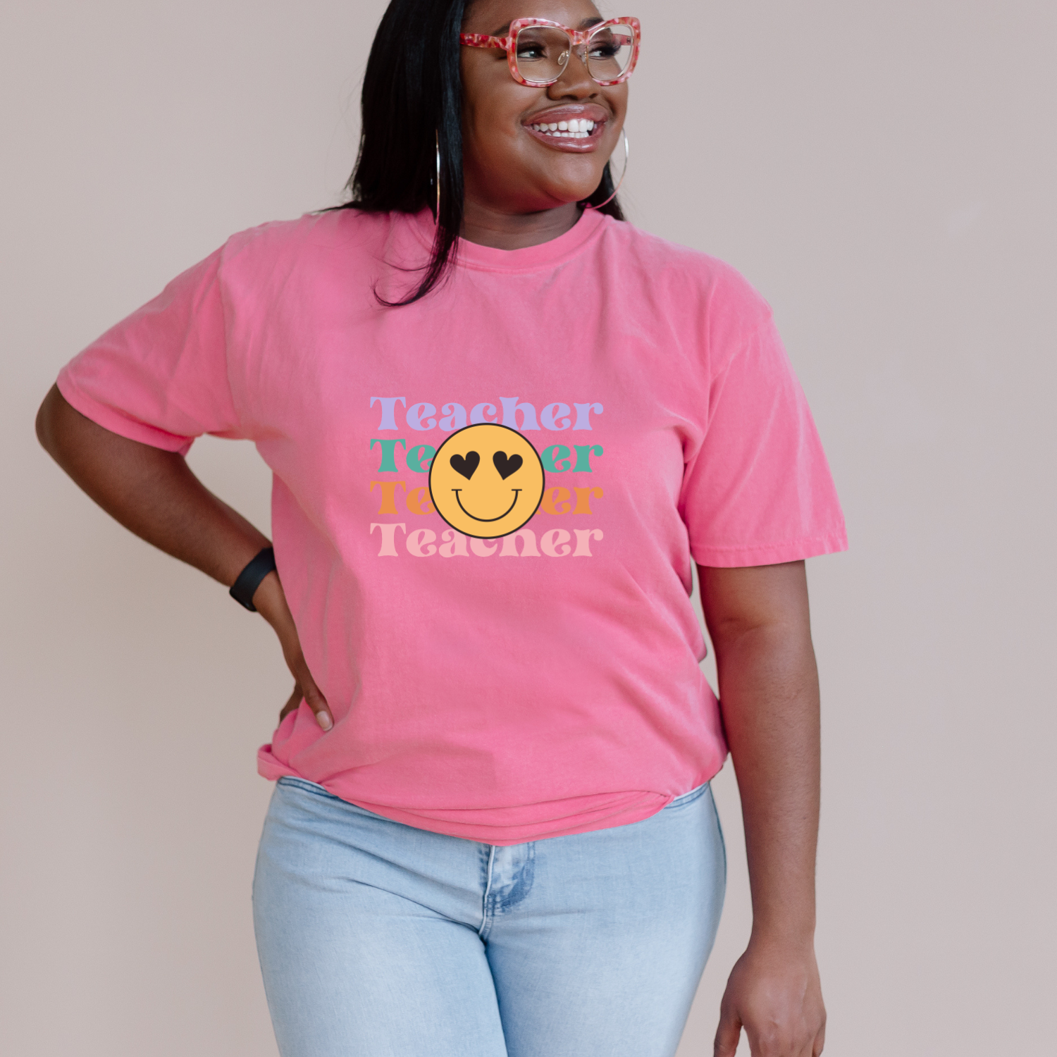 African American woman wearing a pink comfort colors tee with smiley face and teacher text