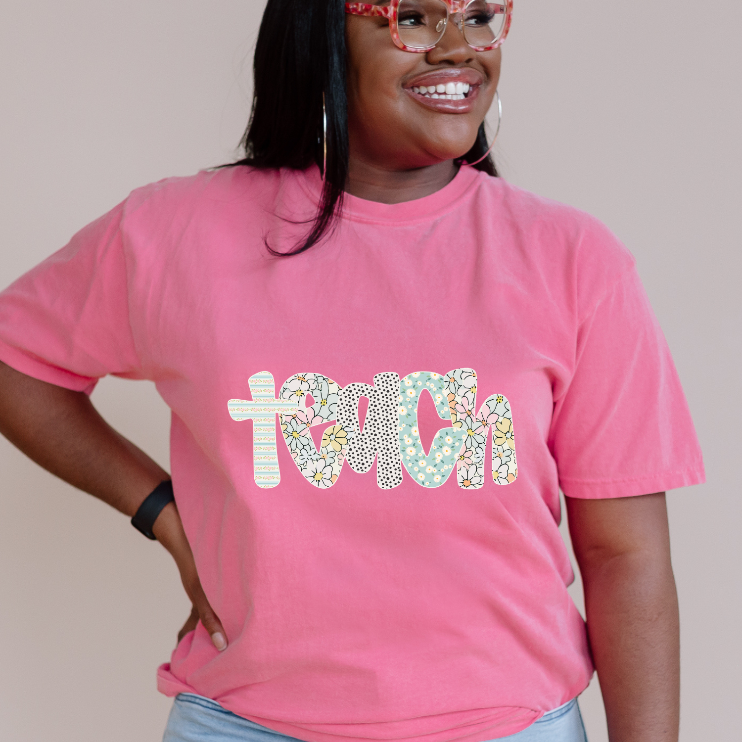 Person wearing a pink t-shirt with 'teach' printed on it, standing against a plain background.
