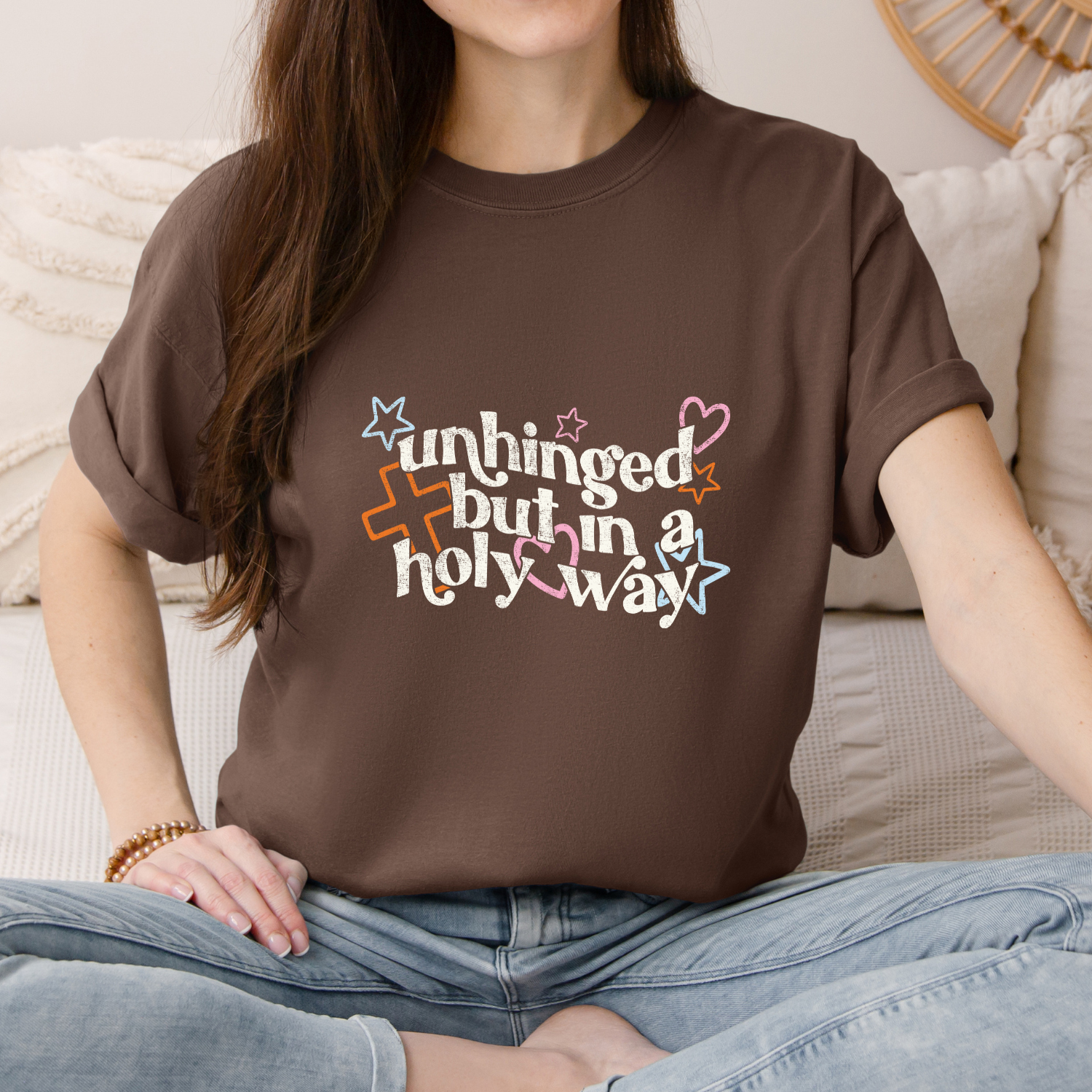 Person wearing a brown t-shirt with colorful text design sitting on a couch.