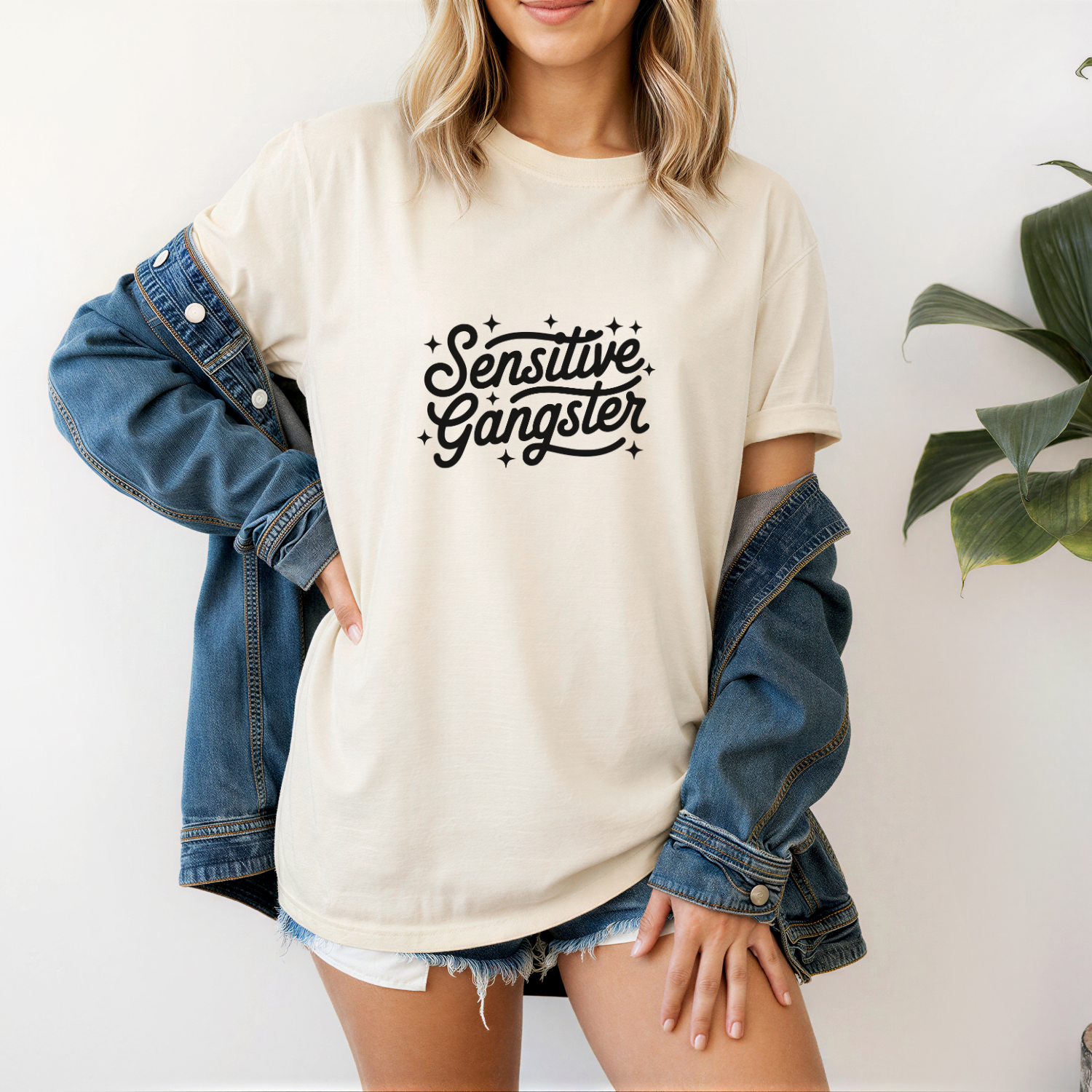 Person wearing a beige t-shirt with 'Sensitive Gangster' text, paired with a denim jacket.