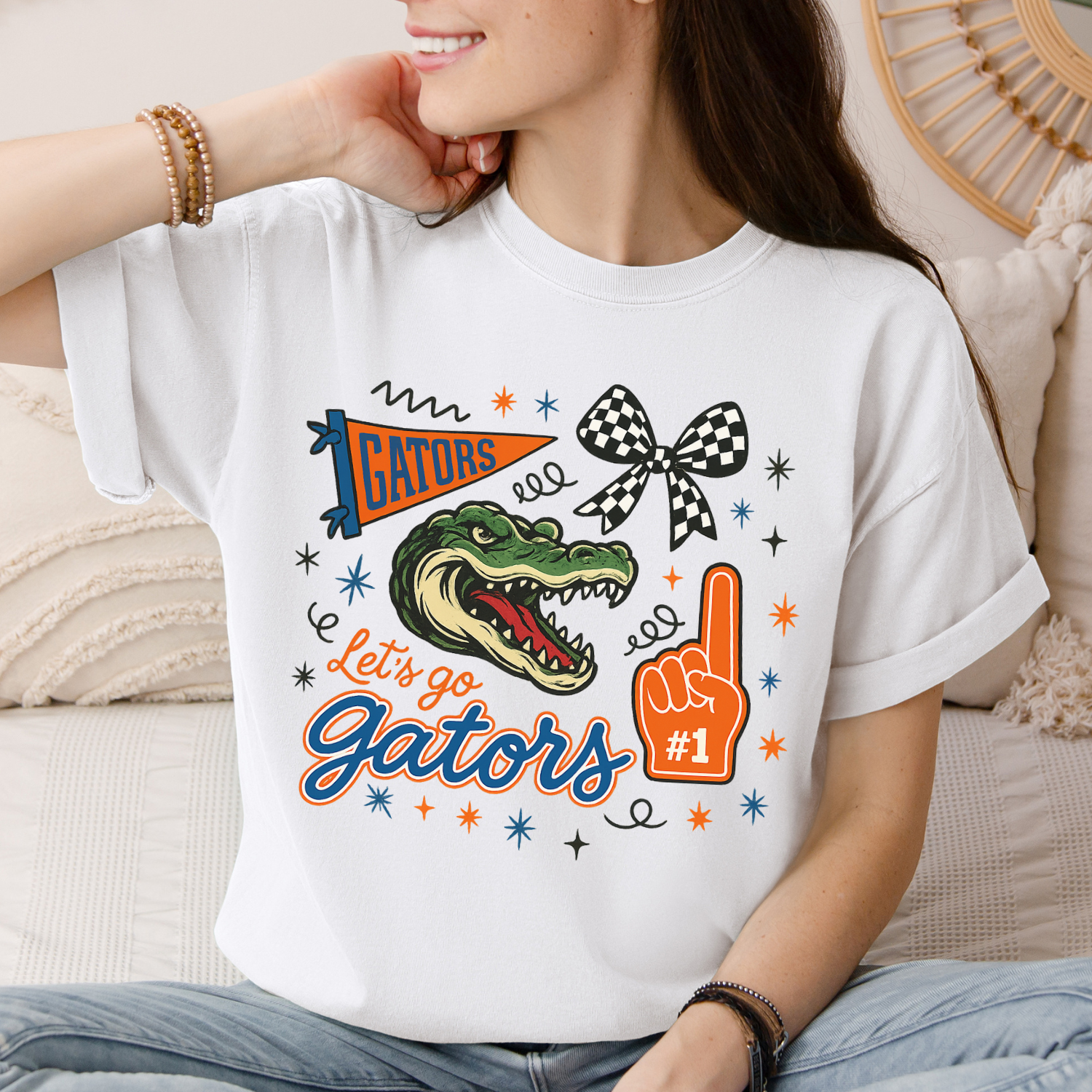 White Florida Gators pride tee with cute alligator, number one sign, checkered bow and text that reads "let's go gators"