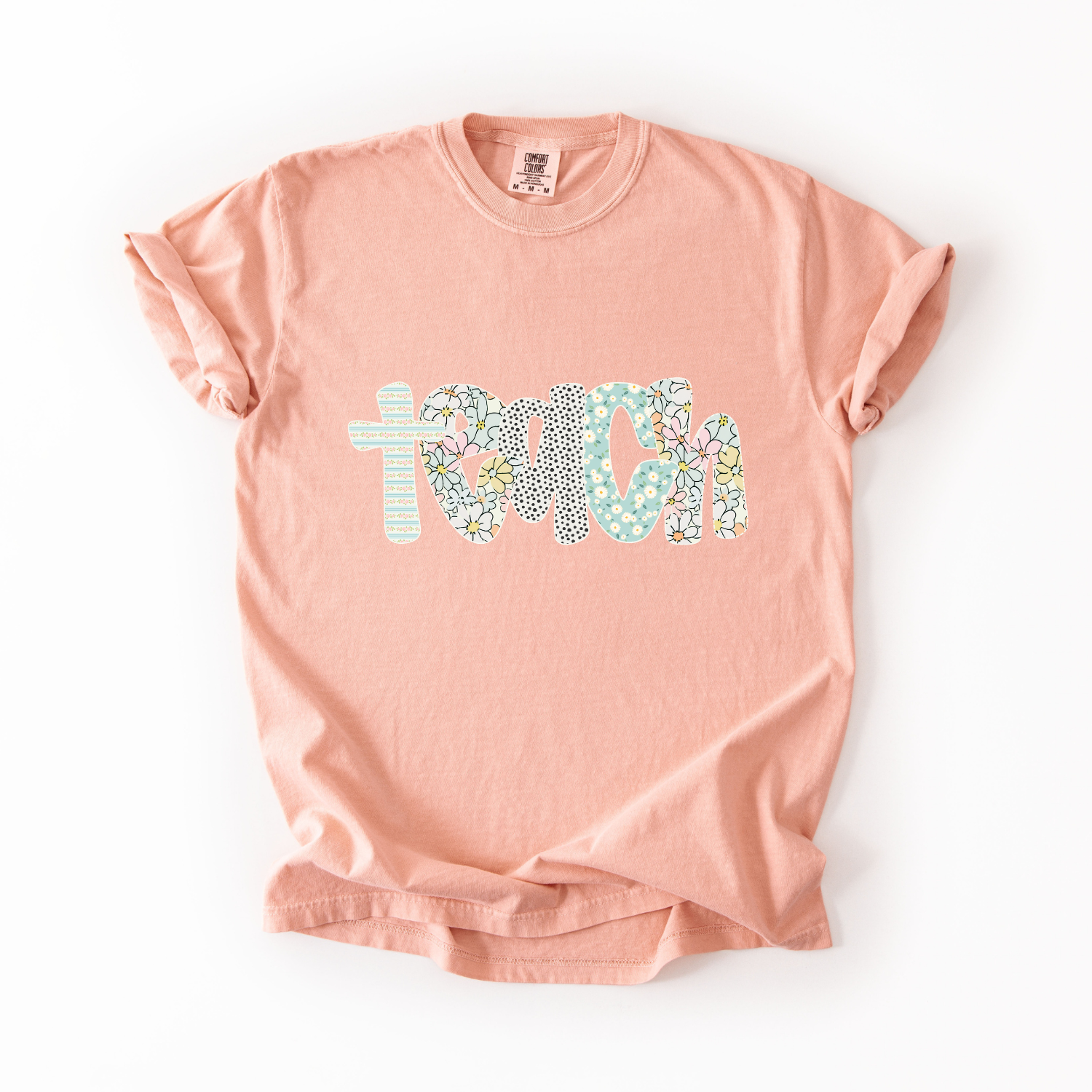 Pink t-shirt with floral lettering on a white background, lettering reads "teach"