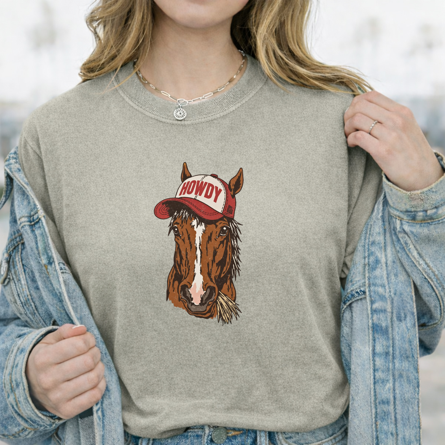 Person wearing a gray sweatshirt with a horse graphic and 'Howdy' hat design, outdoors.
