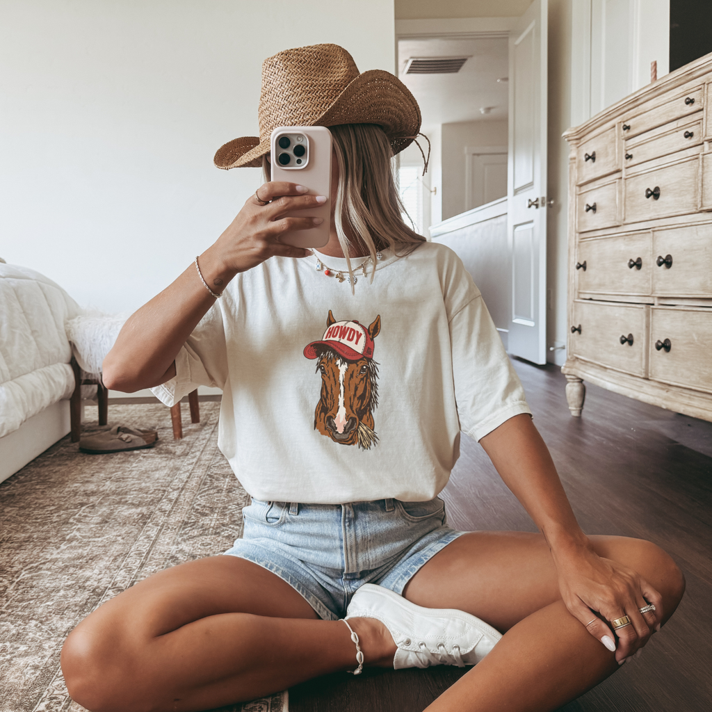 Person wearing a white t-shirt with a horse graphic and text, sitting in a room.