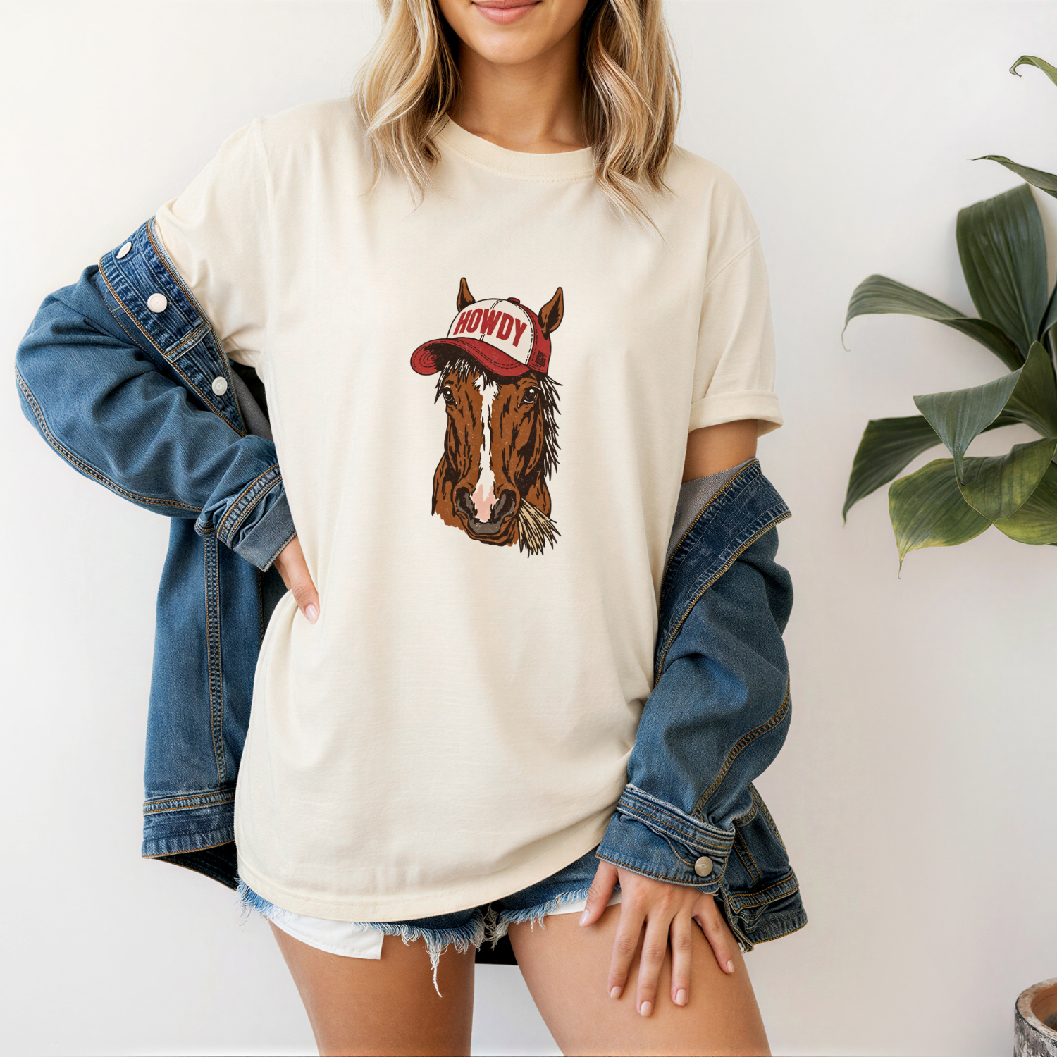 Person wearing a cream t-shirt with a horse graphic and 'Howdy' hat design, standing against a white background.