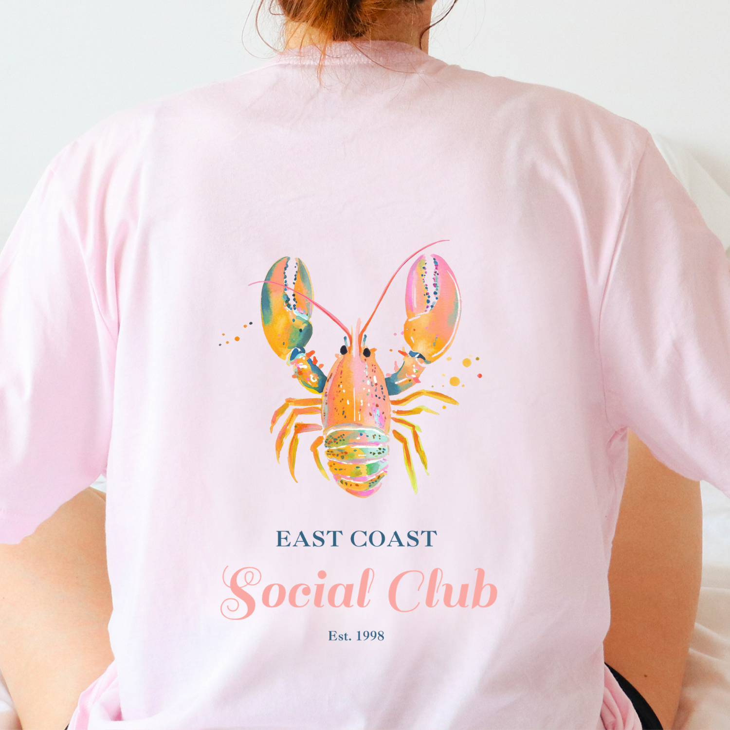 Pink t-shirt back displayed with a colorful watercolor lobster and the words "east coast social club" for a nantucket, coastal styled tshirt