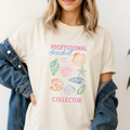 Comfort colors tee in Ivory with vintage seashell drawings in bright pink, orange, blue and green with the text "professional seashell collector"